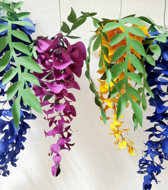 Twelve intricately handcrafted paper wisteria flowers, in a gradient of festive colors, each measuring between 20cm and 30cm, designed to bring the whimsical charm of spring to any celebration or home decor.